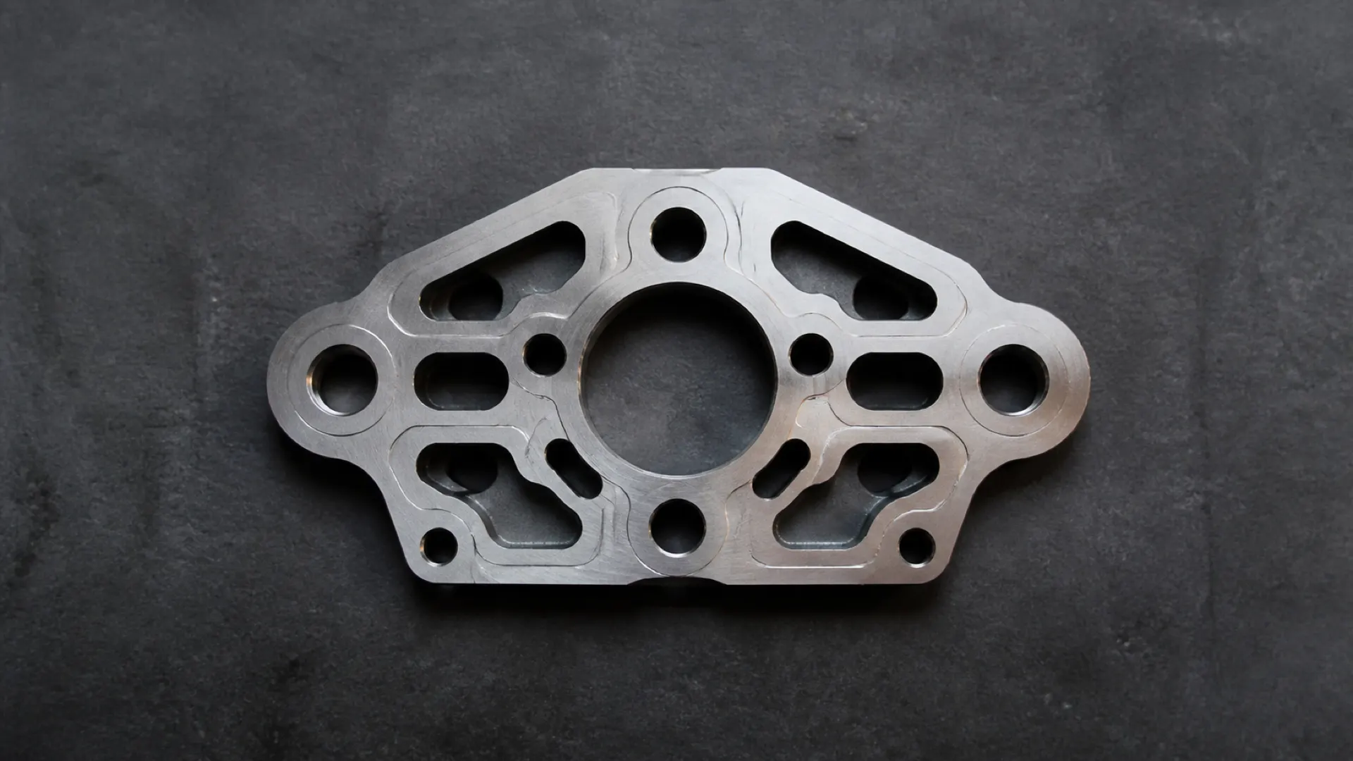 An anonymous precision-machined component on a dark industrial surface